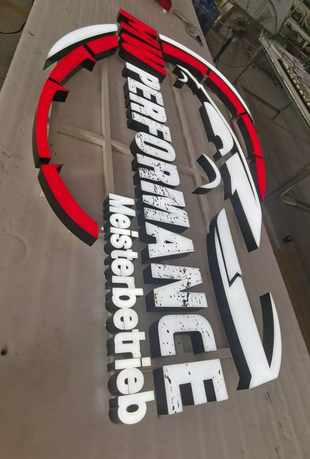 Leuchtbuchstaben und rotes Logo „Performance Meisterbetrieb“ in der Fertigung.