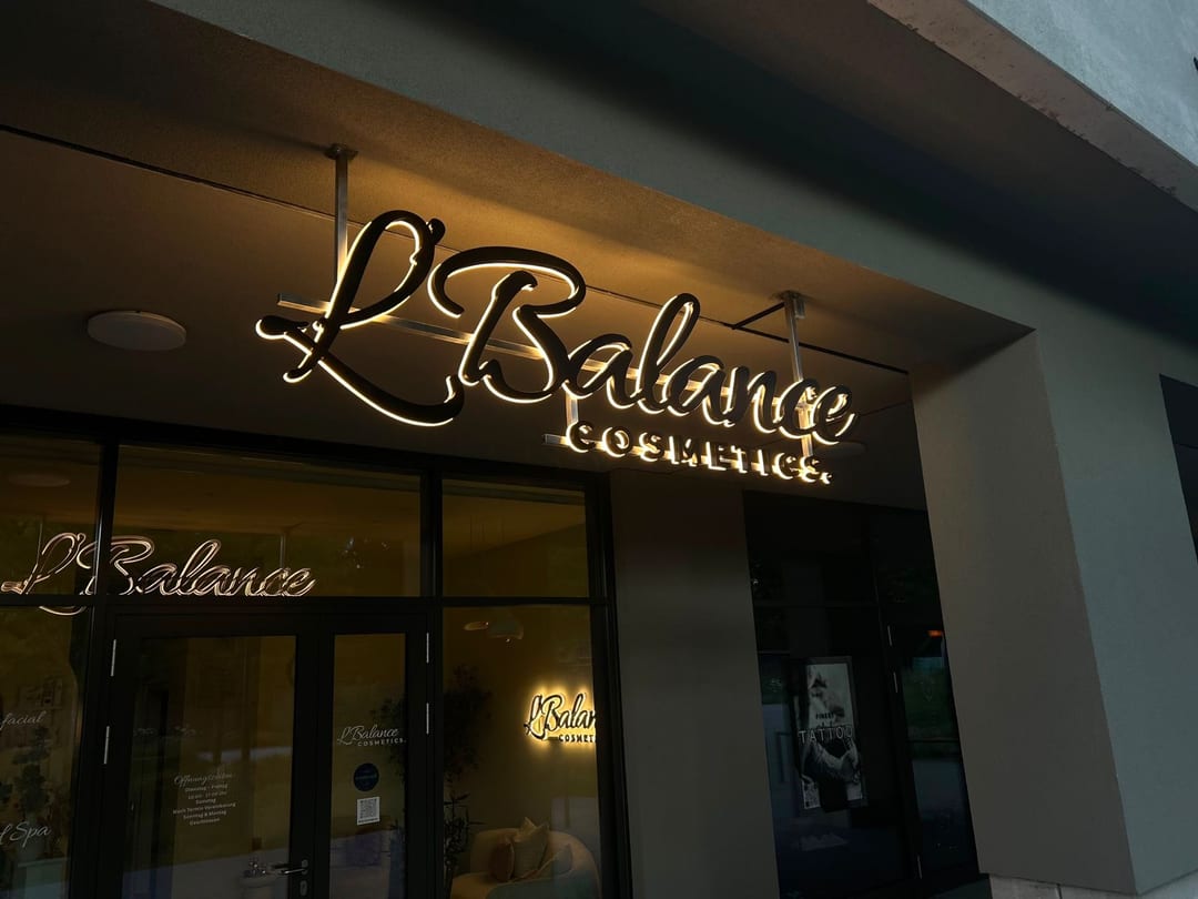 Rückleuchtender Schriftzug „L'Balance Cosmetics“ an der Fassade.