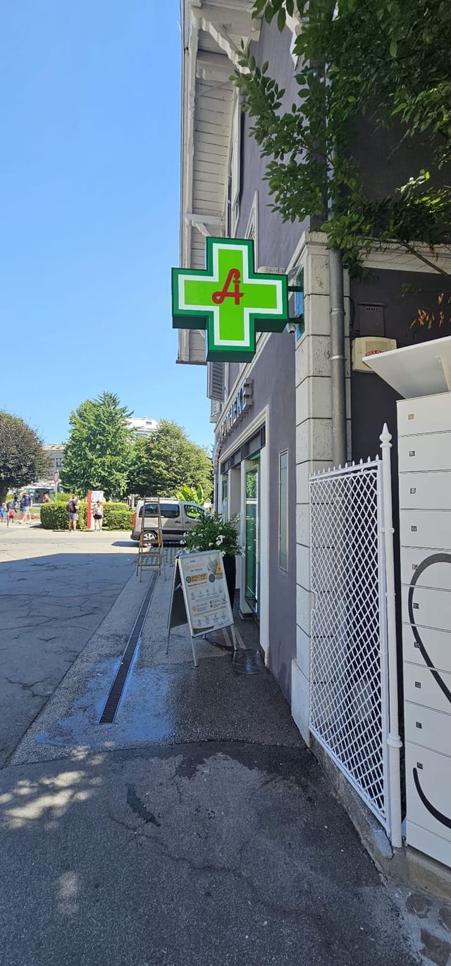 Grün leuchtendes Apothekenkreuz als Ausleger an einer Fassade.
